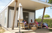 Familie sidder på verandaen i en Beach Loft lodge på Camping Zonneweelde i Holland, omgivet af sommerstemning.