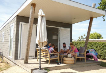 Familie sidder på verandaen i en Beach Loft lodge på Camping Zonneweelde i Holland, omgivet af sommerstemning.