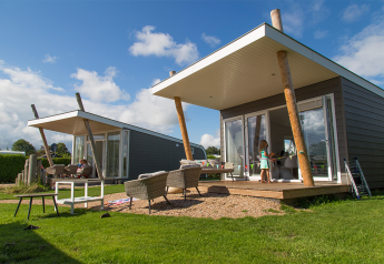 Moderni lodge Beach Loft al Camping Zonneweelde nei Paesi Bassi con terrazza, sedie e tempo soleggiato.