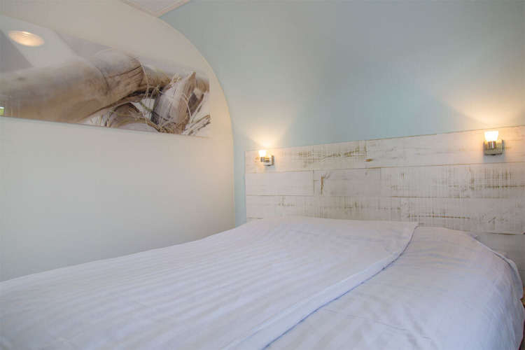 Bright bedroom in the Beach Loft at Camping Zonneweelde, Netherlands, featuring white linens and art.
