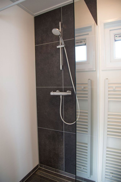 Moderne douche met donkere tegels en glazen wand in de badkamer van Beach Loft op Camping Zonneweelde.