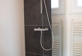 Ducha moderna con baldosas oscuras y mampara de vidrio en el baño del Beach Loft en Camping Zonneweelde.