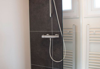 Ducha moderna con baldosas oscuras y mampara de vidrio en el baño del Beach Loft en Camping Zonneweelde.