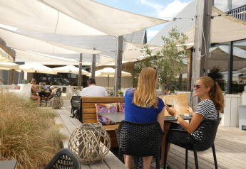 Deux femmes assises en terrasse au Beach Loft du Camping Zonneweelde, Pays-Bas, profitant d'une journée ensoleillée.