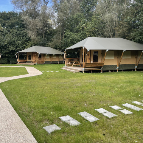 Glampingtent Family en Urban-Gardens, Bélgica; tiendas modernas rodeadas de césped y naturaleza frondosa.