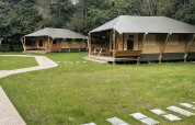 Glampingtent Family en Urban-Gardens, Bélgica; tiendas modernas rodeadas de césped y naturaleza frondosa.