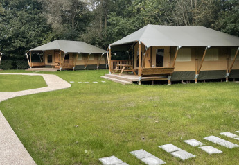 Glampingtent Family en Urban-Gardens, Bélgica; tiendas modernas rodeadas de césped y naturaleza frondosa.