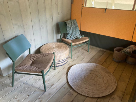 Acogedor rincón en Glampingtent Family - Gent en Bélgica con sillas, alfombras y cestos de mimbre.