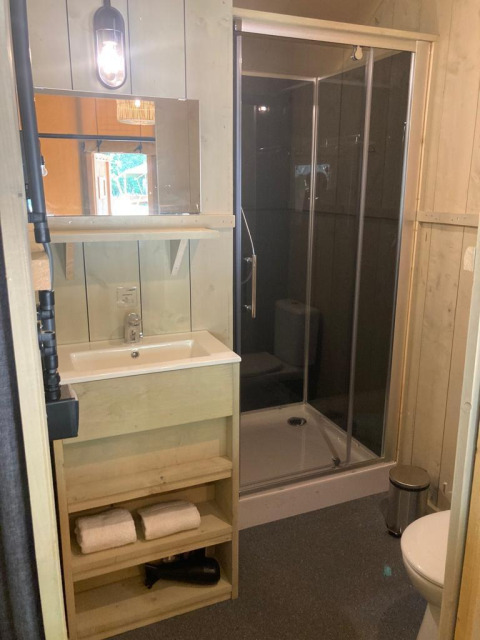 Baño de madera moderno con ducha, lavabo, espejo, toallas y aseo en Glampingtent Family en Bélgica.