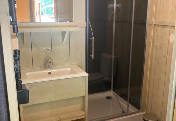 Baño de madera moderno con ducha, lavabo, espejo, toallas y aseo en Glampingtent Family en Bélgica.