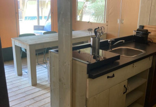Vista de la cocina y comedor de una cómoda tienda glamping con muebles de madera en Urban-Gardens, Bélgica.