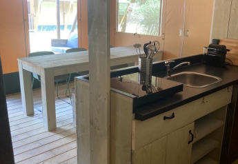 Vista de la cocina y comedor de una cómoda tienda glamping con muebles de madera en Urban-Gardens, Bélgica.