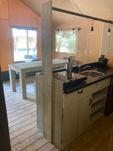Vista de la cocina y comedor de una cómoda tienda glamping con muebles de madera en Urban-Gardens, Bélgica.