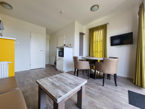 Gezellige leefruimte met eettafel, vier stoelen, wand-tv en houten vloer in Comfort Lodge Nieuwpoort.