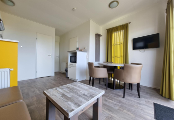 Zona giorno luminosa con tavolo da pranzo, quattro sedie, TV a parete e pavimento in legno al Comfort Lodge Nieuwpoort.