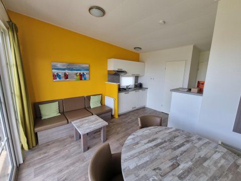 Woonruimte van Comfort Lodge op Kompas Camping Nieuwpoort, België, met moderne keuken, zetel en eettafel.