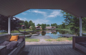 Gezicht vanaf een overdekt terras op een meer met steigers en sfeervolle glamping hutten in het groen.