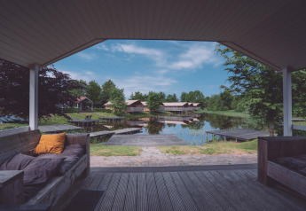 Vue d’une terrasse couverte sur un lac avec pontons, cabanes de glamping et nature verdoyante autour.