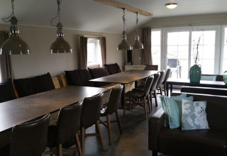 Eetruimte met grote tafels en stoelen in de groepslodge bij Holiday park Eigen Wijze, Nederland, helder interieur.