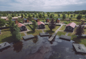 Glamping-ophold med små hytter ved en sø, grønne omgivelser og trædæk til afslapning i naturen.