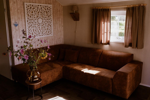 Living room at Group lodge in Holiday park Eigen Wijze, Netherlands, with brown sofa and flower vase.