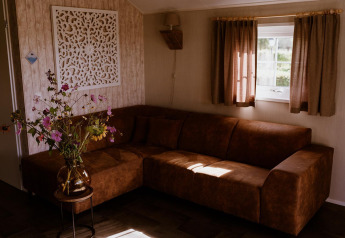 Living room at Group lodge in Holiday park Eigen Wijze, Netherlands, with brown sofa and flower vase.