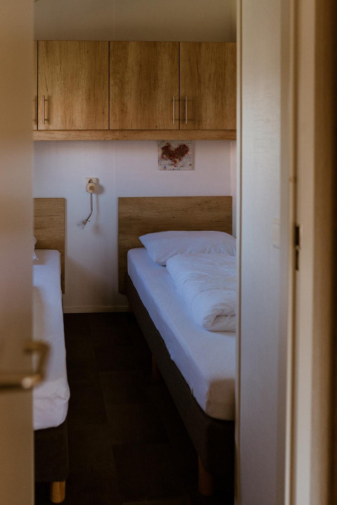 Habitación con dos camas individuales, armarios de madera y ropa de cama en Group lodge, Holiday park Eigen Wijze, Países Bajos.