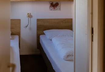 Zimmer mit zwei Einzelbetten, Holzschränken und Bettwäsche in der Group lodge im Holiday park Eigen Wijze, Niederlande.