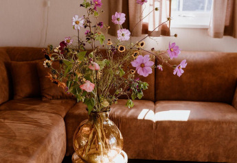 Bouquet champêtre dans un vase en verre ambré sur table près d’un canapé, salon d’un lodge néerlandais éclairé.