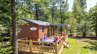 Famille attablée sur la terrasse d’un cottage à Veluwecamping De Pampel, entourée de forêt verdoyante.