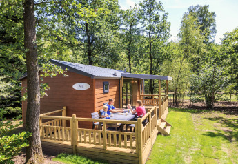 Familie sidder udenfor på terrassen ved Cottage på Veluwecamping De Pampel, omgivet af frodig skov.
