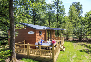 Gezin geniet op het terras van een cottage bij Veluwecamping De Pampel, omgeven door groene bossen.
