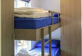 Habitación con litera, sábanas azules, edredones, armario y ventana en la cabaña de Veluwecamping De Pampel, Países Bajos.