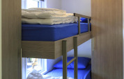 Habitación con litera, sábanas azules, edredones, armario y ventana en la cabaña de Veluwecamping De Pampel, Países Bajos.
