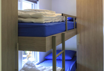 Chambre avec lit superposé, draps bleus, couettes, armoire et fenêtre au Cottage du Veluwecamping De Pampel, Pays-Bas.