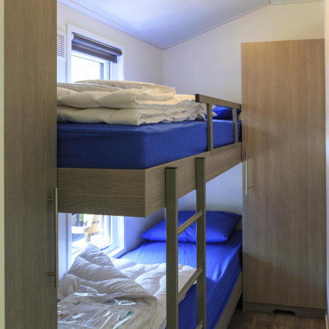 Værelse med køjeseng, blå lagner og dyner, skab og vindue i en hytte på Veluwecamping De Pampel, Holland.