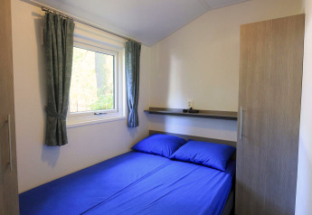 Cozy bedroom with blue sheets in a cottage at Veluwecamping De Pampel, Netherlands, featuring a window view.