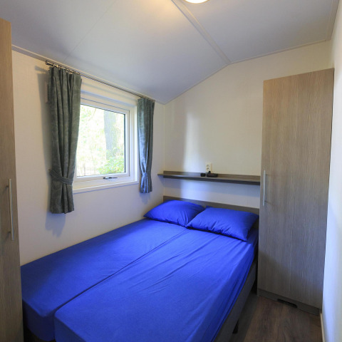 Petite chambre avec literie bleue dans un cottage à Veluwecamping De Pampel aux Pays-Bas, avec fenêtre.