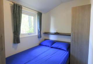 Cozy bedroom with blue sheets in a cottage at Veluwecamping De Pampel, Netherlands, featuring a window view.