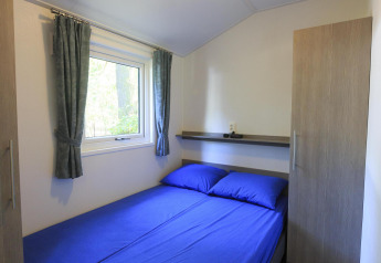 Cozy bedroom with blue sheets in a cottage at Veluwecamping De Pampel, Netherlands, featuring a window view.