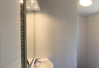 Salle de bain moderne avec lavabo, miroir et carrelage blanc au Cottage de Veluwecamping De Pampel, Pays-Bas.