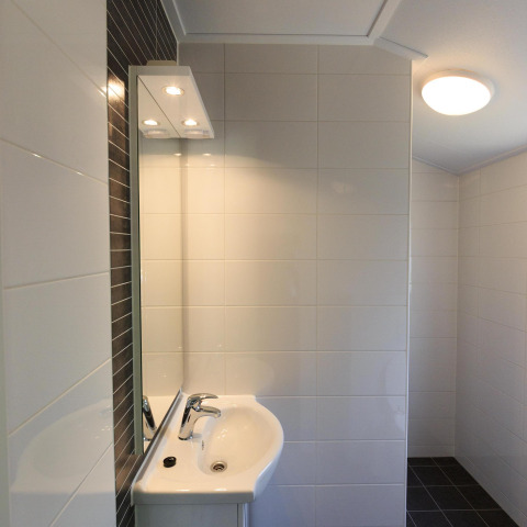 Lavabo moderno con espejo, azulejos blancos y luz de techo en la cabaña de Veluwecamping De Pampel, Países Bajos.