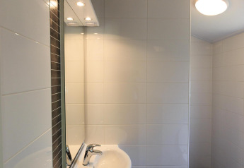 Lavabo moderno con espejo, azulejos blancos y luz de techo en la cabaña de Veluwecamping De Pampel, Países Bajos.