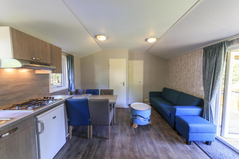 Intérieur d’un chalet au Veluwecamping De Pampel, Pays-Bas, avec cuisine moderne et canapé bleu.