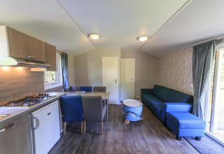 Interior de una cabaña en Veluwecamping De Pampel, Países Bajos, con cocina moderna y sofá azul.