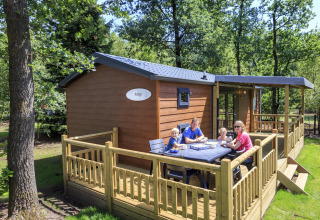 Familie sidder og spiser morgenmad på træterrassen ved en hytte på Veluwecamping De Pampel i Holland.