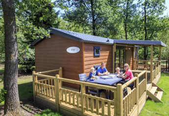 Familie sidder og spiser morgenmad på træterrassen ved en hytte på Veluwecamping De Pampel i Holland.