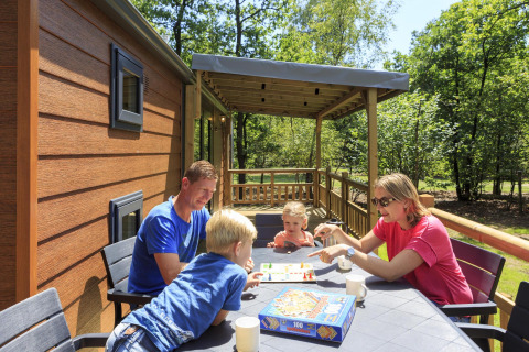 Familie nyder et brætspil udendørs på terrassen ved Cottage på Veluwecamping De Pampel, Holland.