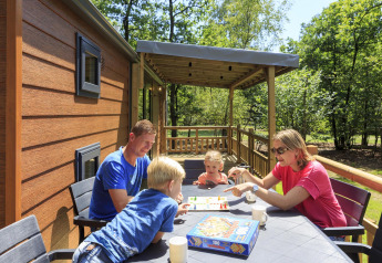 Familie nyder et brætspil udendørs på terrassen ved Cottage på Veluwecamping De Pampel, Holland.