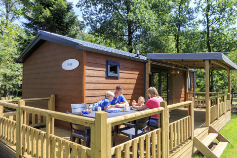 Family enjoying a meal outside a wooden lodge at Cottage in Veluwecamping De Pampel, Netherlands.
